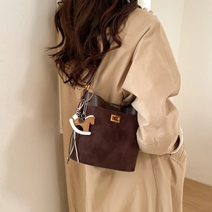 Detail showing the brown suede texture and golden square twist lock on the bucket bag