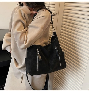 Détail d'un grand sac bandoulière noir avec zips argentés porté par un mannequin