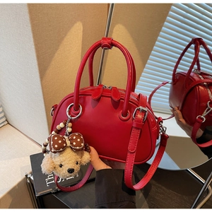 Detailed view of red Boston bag featuring a plush bear charm and dual zippers