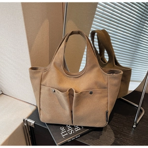 Detail of khaki canvas tote bag featuring double front pockets and metal buckles