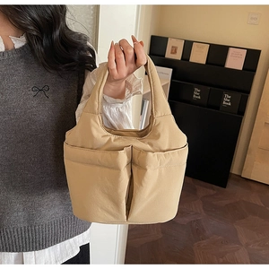 Close-up of quilted beige bucket bag with large front pockets held by a model