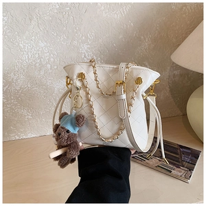 Detail of white quilted bucket bag with gold chain strap and brown bear charm accessory
