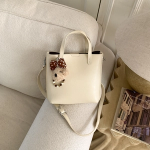 Détail du sac seau en cuir blanc cassé avec breloque ours sur un canapé confortable
