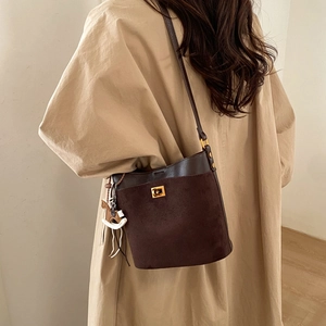 Detailed back view of a brown suede and leather bucket bag on a beige trench coat