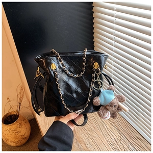 Close-up of black quilted bucket bag with gold chain strap and a blue teddy bear pendant