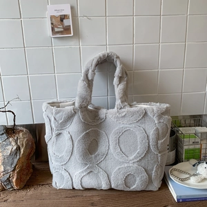 Close-up of light grey plush tote bag with circular embossed patterns on wooden table