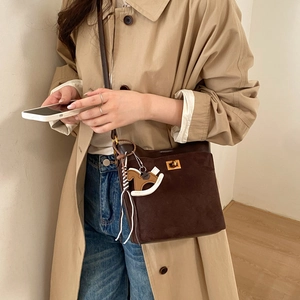 Detailed close-up of dark brown suede bucket bag featuring a gold metal buckle and horse charm
