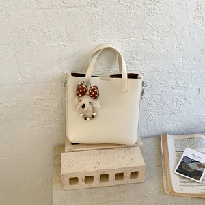 Détail du sac seau crème minimaliste avec breloque caniche et bandoulière chaîne