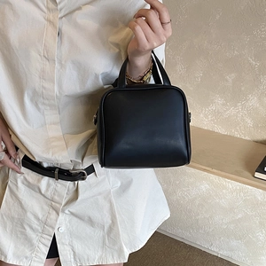 Fashionable black faux leather handbag held by model in minimalist lifestyle setting