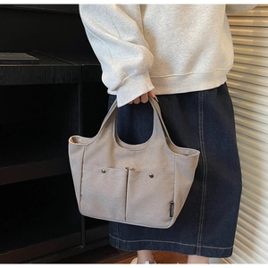 Detail of grey canvas tote bag with front pockets and silver metal buckle accents