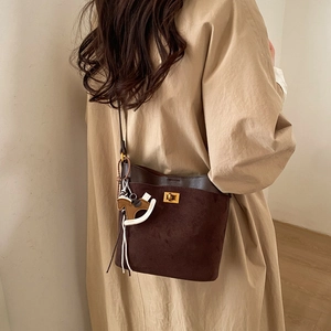 Detail of dark brown suede bucket bag with gold clasp and horse charm on beige coat