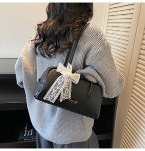 Detail of black pebbled leather Boston bag with white lace bow charm on grey sweater