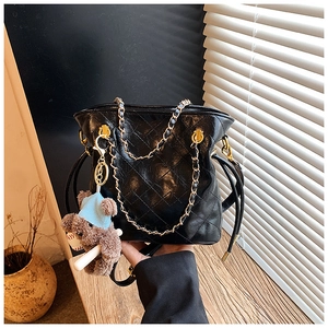 Detail of black quilted bucket bag with gold chain strap and cute bear charm accent