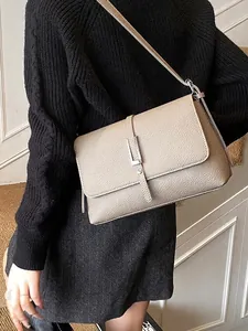 Minimalist beige pebble leather square crossbody bag with silver buckle worn by a model