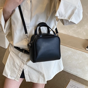 Detail shot of a minimalist black crossbody bag on a white shirt with silver metal hardware