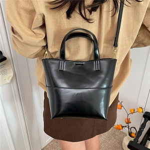 Dettaglio di una borsa a secchiello nera lucida con hardware dorato e tracolla