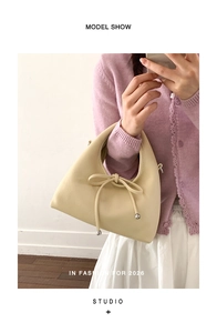 Close-up of beige satchel bag featuring decorative bow tie and gold metal charm detail