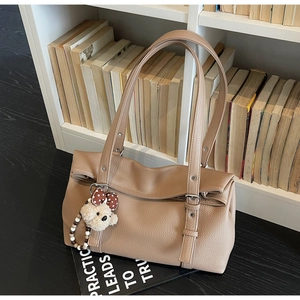 Close-up of camel leather tote bag with a cute plush bear charm in front of a bookshelf