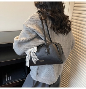 Detail of black leather Boston bag featuring a white lace bow and golden brand logo