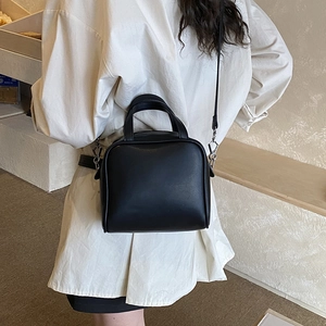 Close-up of matte black leather mini square handbag with structured top handle and strap