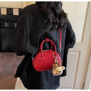 Detail shot of a red leather bowling bag with a cute bear charm on a model's shoulder