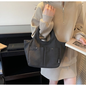 Close-up of a dark grey canvas handbag with front pockets and elegant metal fasteners