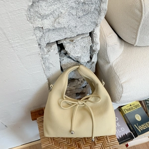 Close-up of cream leather handbag featuring a drawstring bow and silver metal hardware