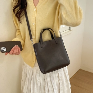 Sac seau en cuir marron foncé minimaliste porté sur un cardigan en maille claire