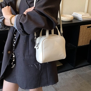 Detail shot of a minimalist white leather crossbody bag with metallic strap hardware