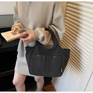 Detailed side view of a black canvas tote bag with front pockets and silver buckle accents