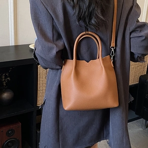 Close-up of caramel brown pebble leather tote bag with cylindrical handles and logo detail