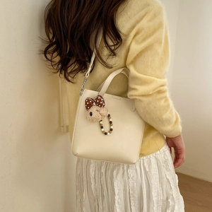 Détail d'un sac seau blanc crème avec pendentif ours en peluche et texture de cuir souple