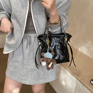 Detail of black quilted leather bucket bag with gold chain strap and cute bear charm