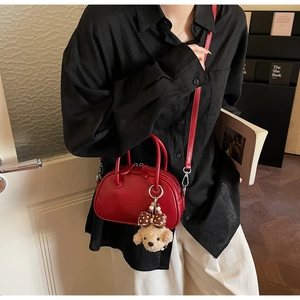 Detail of red leather bowling bag with cute bear charm worn by a model in casual style