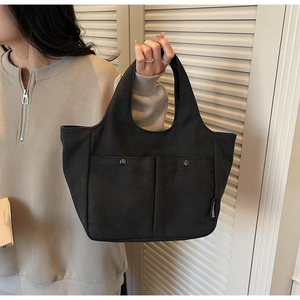 Detail view of black canvas tote bag showing front pockets and metal buckle on the surface