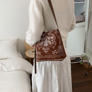 Détail de broderie bohème sur sac seau en daim marron porté par un mannequin