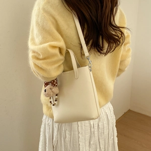 Détail du sac seau en cuir crème avec charm ours brun et bandoulière amovible