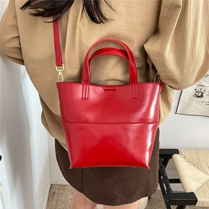 Dettaglio di una borsa tote rossa lucida con finiture dorate e tracolla rimovibile