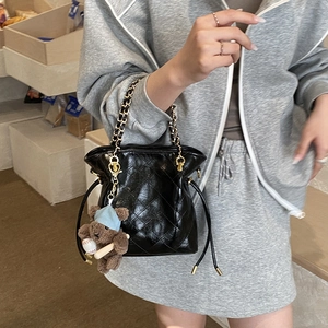 Detail of black quilted bucket bag with chain strap and cute teddy bear charm