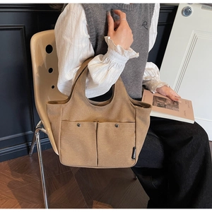 Close-up of khaki canvas tote bag featuring double front pockets with metal snap buttons