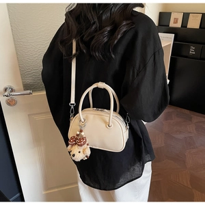 Detail of cream bowling bag with plush teddy bear charm and adjustable strap worn by model