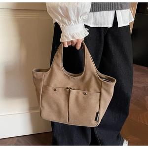 Detail of a brown canvas handbag featuring large front pockets and metallic rivets