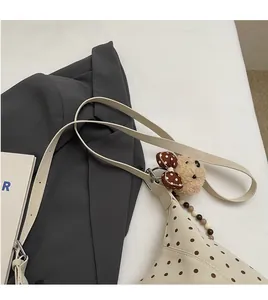 Close-up of minimalist beige polka dot shoulder bag with cute bear charm and bead chain