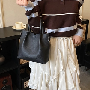 Detail of black pebbled leather tote bag with V-cut edge held by model in casual setting