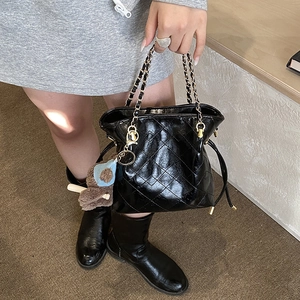 Detailed close-up of a black quilted bucket bag with golden chain and plush bear charm