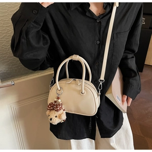 Close-up of beige semi-circular handbag with plush puppy charm and adjustable strap