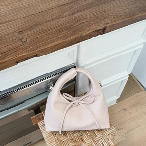 Detail of light pink lychee leather handbag with decorative bow on a woven stool