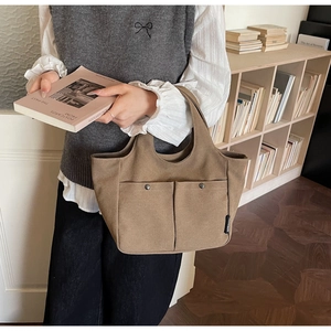 Detail of khaki canvas tote bag featuring dual front metal buckle pockets and side woven label