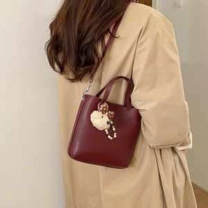 Détail du sac seau bordeaux sur mannequin avec pendentif d'ours en peluche mignon et chic