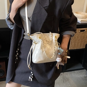 Detail showing white quilted bucket bag with chain strap and a brown teddy bear charm